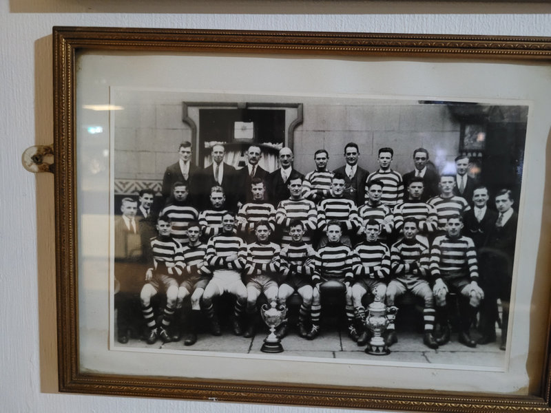 Early Higginshaw team photo in hooped shirts, with two trophies