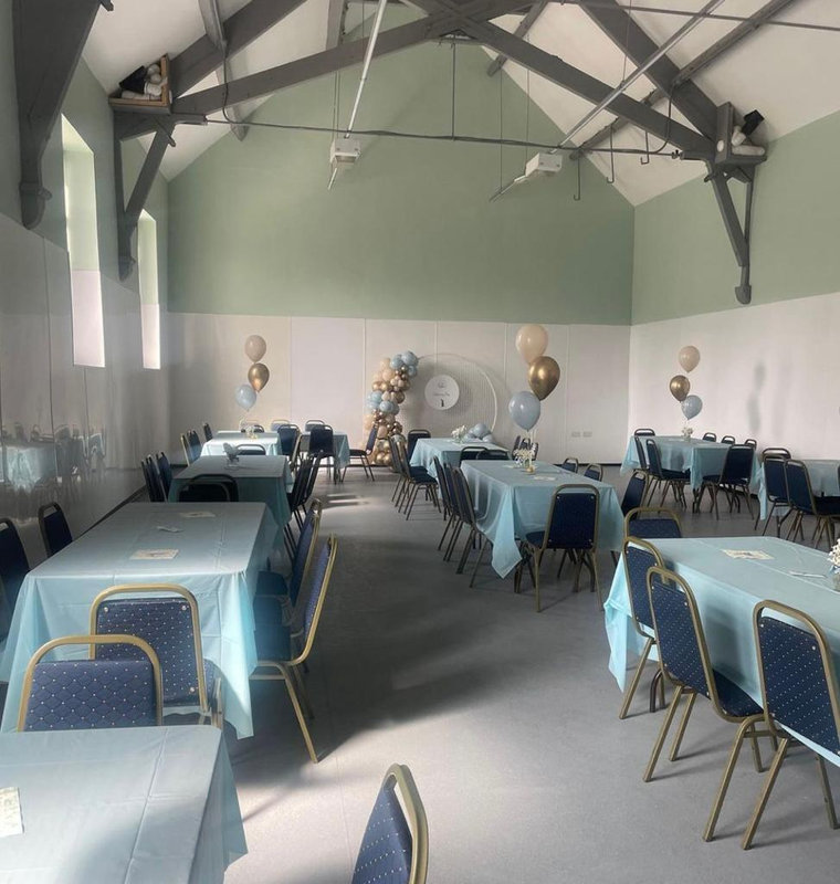 The hall set up for a party, with blue tablecloths and balloons